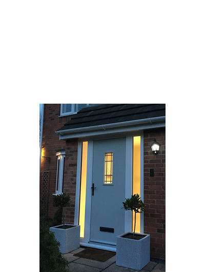 Light coloured composite front door with twin side panels at night